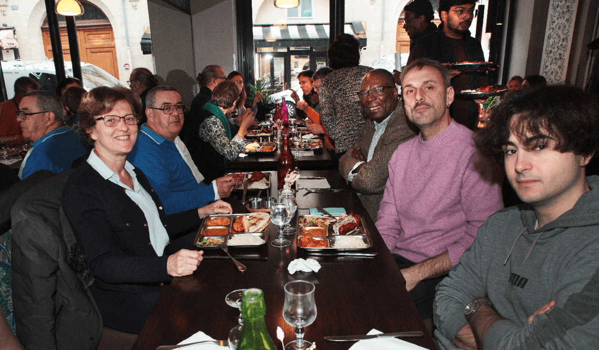 Membres de l'association assis à table dont Ferdinand Ezembé, le fondateur de l'association et Agnès Ostertag, membre du bureau de l'association lors du repas de fin d'année 2025 de l'association Axes Pluriels