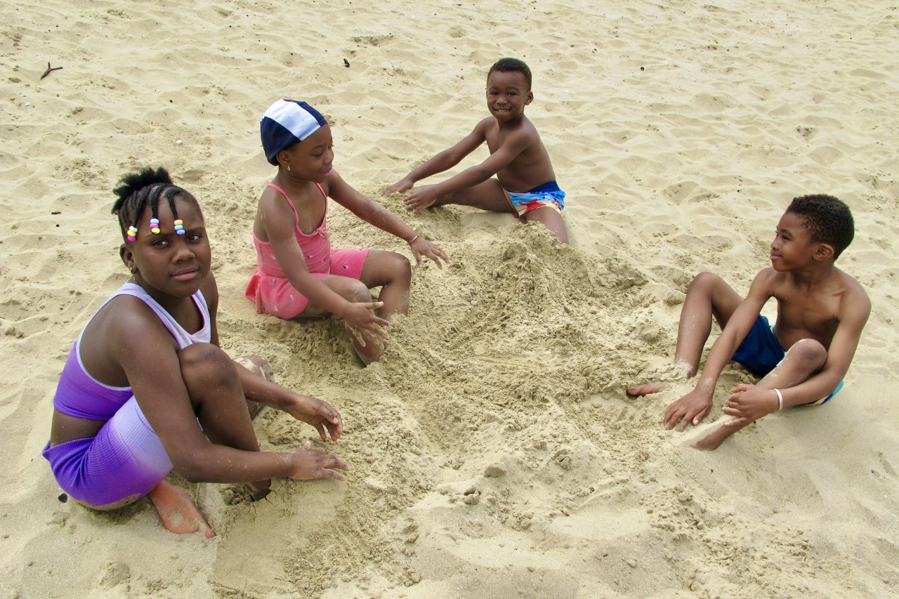 enfants usagers noirs de l'association qui jouent dans le sable à la mer et sourient
