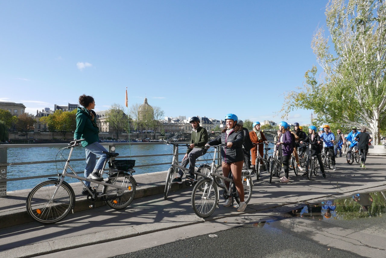 Usagers de l'association sur leurs vélos de location au bord de la Seine, attendant que tout le monde soit prêts et équipés pour commencer la sortie en vélo à Paris