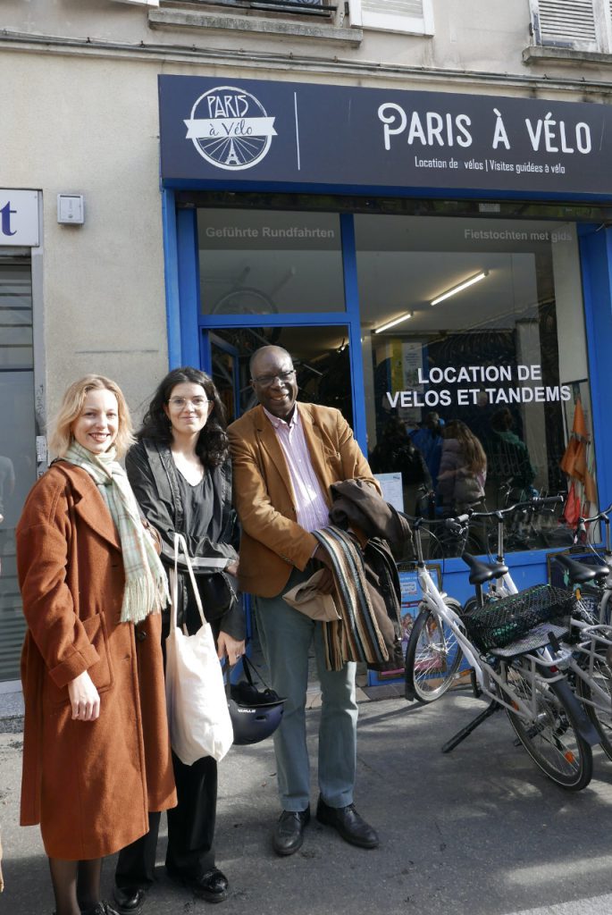 2 femmes migrantes posant pour la photo avec Ferdinand EZEMBE devant la boutique de location de vélo