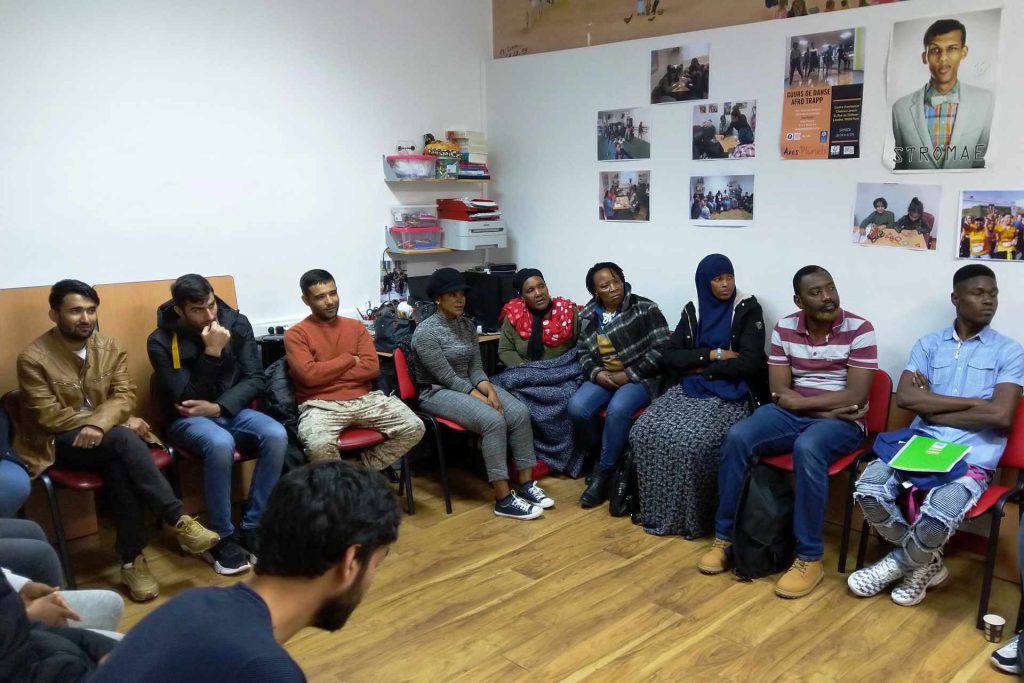 immigrés usagers de l'association assis et à l'écoute dans les locaux d'Axes Pluriels