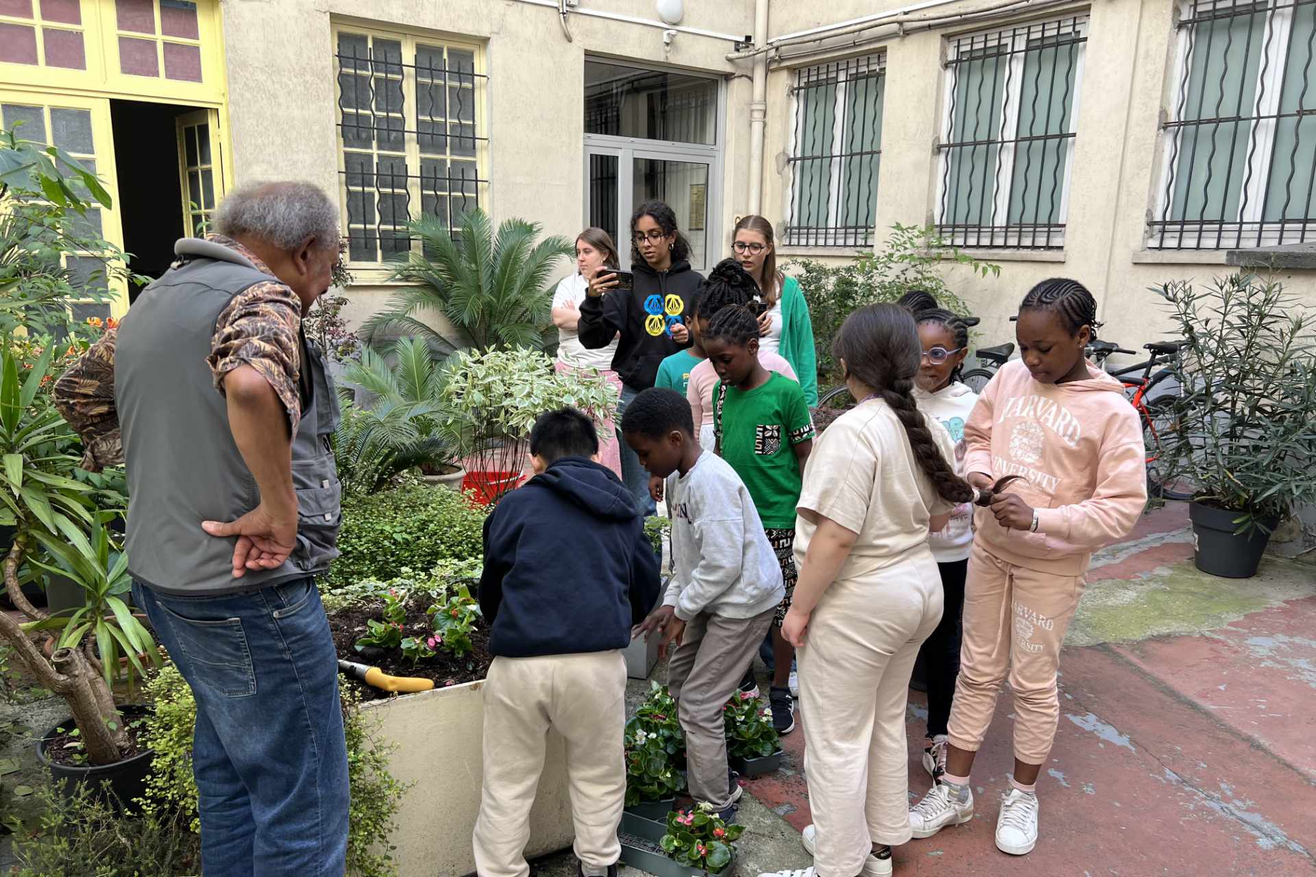 Groupe d'enfants de l'association avec un jardinier qui regardent des plantes de la cour de l'immeuble de l'association