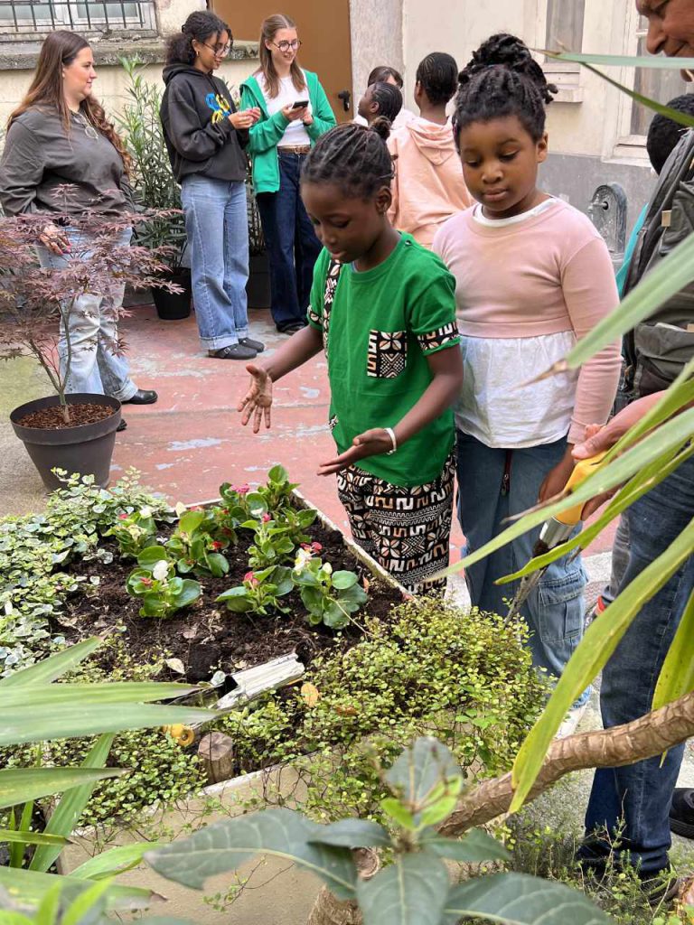 deux jeunes enfants de l'association qui observent les plantes qu'ils viennent de planter dans un pot de la cour de l'immeuble de l'association