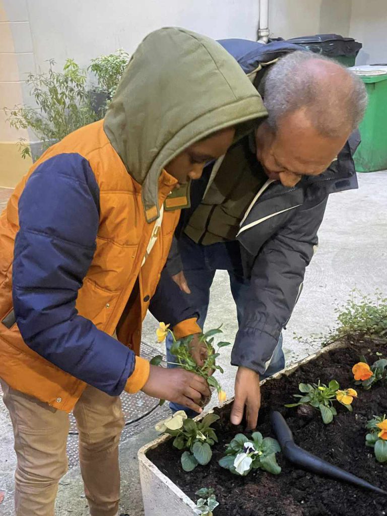 un jeune garçon qui aide le jardinier à mettre des fleurs dans les pots de la cour de l'association