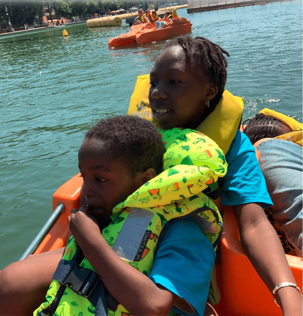 deux enfants noirs qui portent des gilets de sauvetages dans un pédaleau sur le bassin de la Villette à Paris